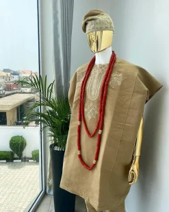 A champagne gold aso oke dashiki, with a floral and ancient style shaped embroidery design, hand woven Yoruba hat, an extra length red and gold coral bead.