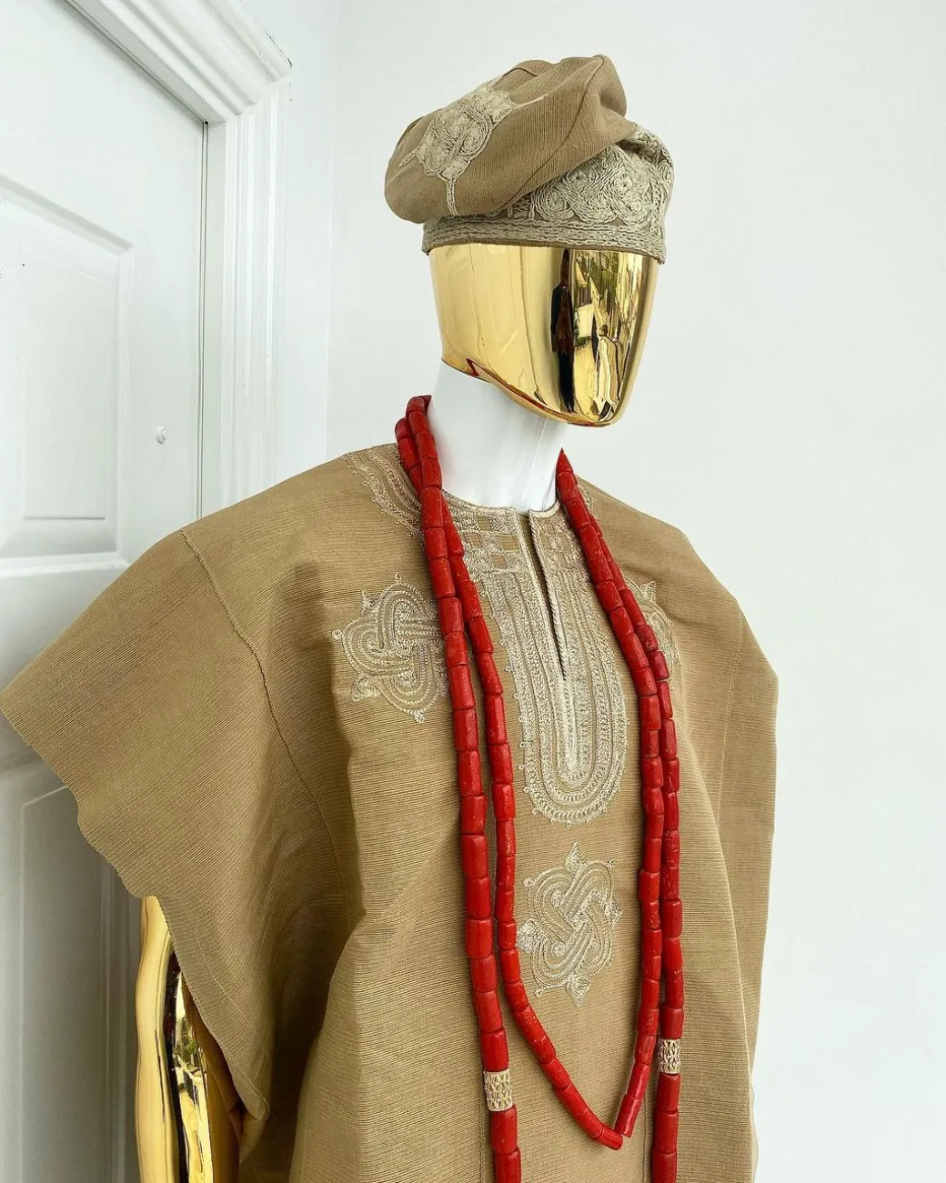 A champagne gold aso oke dashiki, with a floral and ancient style shaped embroidery design, hand woven Yoruba hat, an extra length red and gold coral bead.