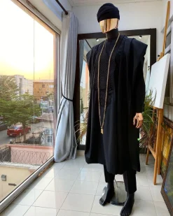 A charcoal black agbada, Jesus piece long fashion chain and hand woven aso oke Yoruba hat.