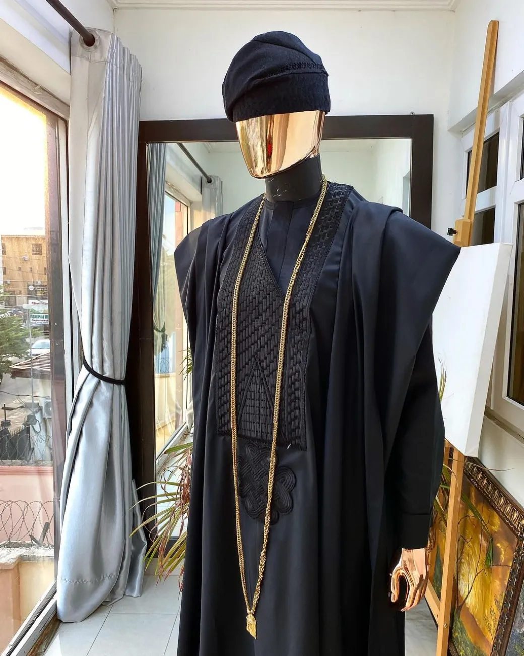 A charcoal black agbada, Jesus piece long fashion chain and hand woven aso oke Yoruba hat.