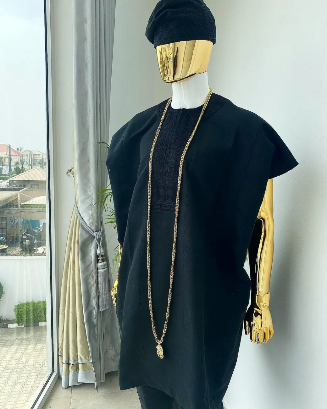 A charcoal black aso dashiki with a floral and box-shaped embroidery design, a hand-weaved Yoruba hat, and a gold Jesus timepiece