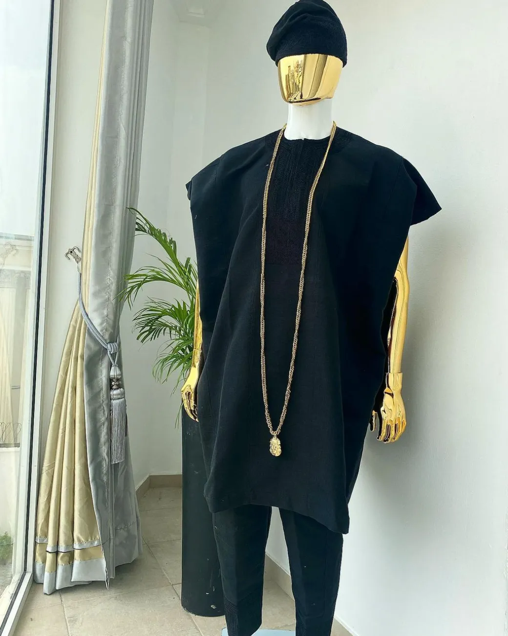 A charcoal black aso dashiki with a floral and box-shaped embroidery design, a hand-weaved Yoruba hat, and a gold Jesus timepiece