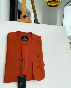 A fire orange, double vertical flap with horizontal closed detailing, combat pocket, and Swarovski button details African traditional senator kaftan native